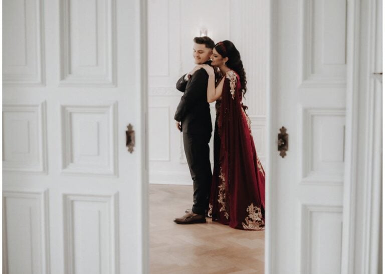 Braut in rotem Hochzeitskleid umarmt den Bräutigam in einem eleganten Raum