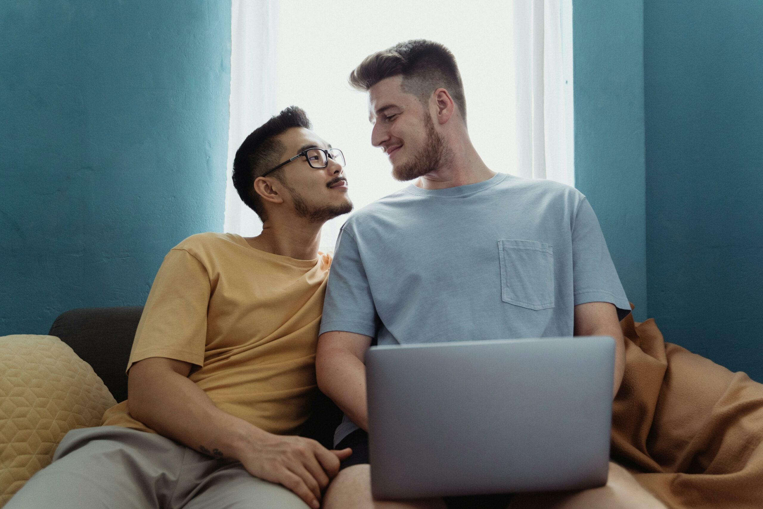 Same sex couple looking at each other as they build a wedding website on their laptop