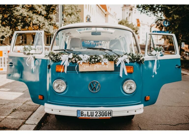 Blauer VW-Bulli mit „Just Married“-Schild und Blumendekoration als Hochzeitsauto