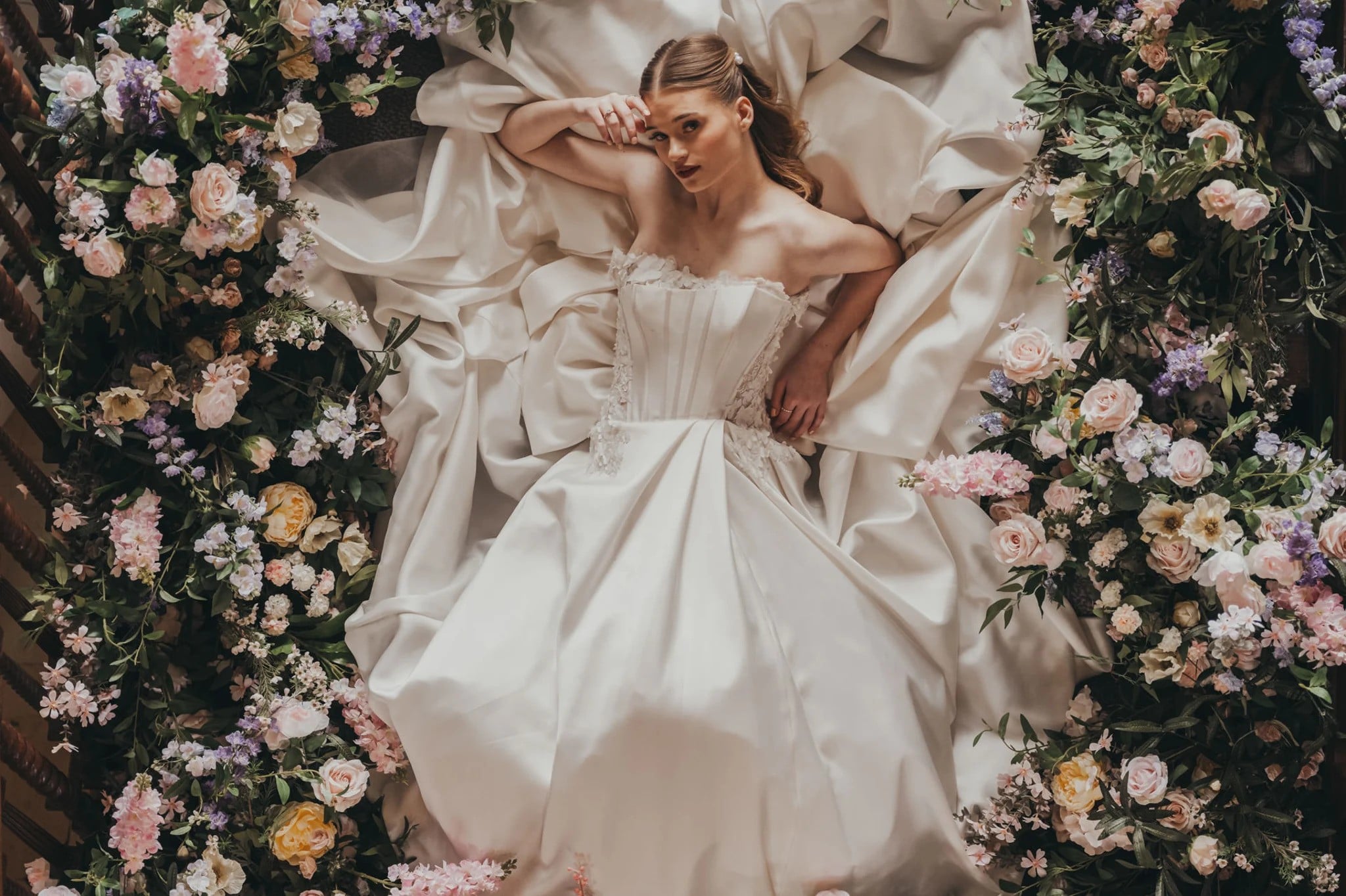 Gen Z bride posing in a basque waist wedding dress in a bed of flowers