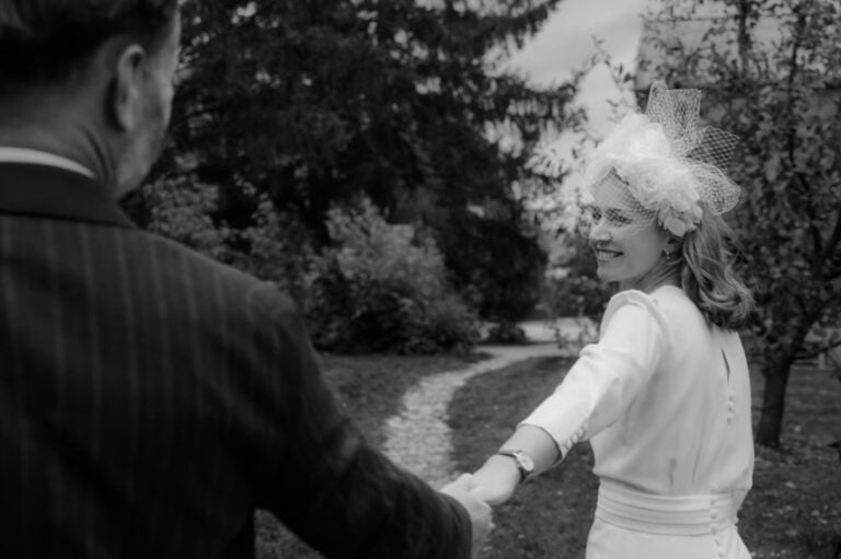 Braut führt Bräutigam lächelnd an der Hand durch einen Garten bei der Hochzeit