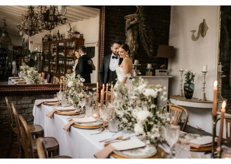 Braut und Bräutigam stehen in einer romantisch dekorierten Hochzeitslocation mit elegant gedecktem Hochzeitstisch und Blumen