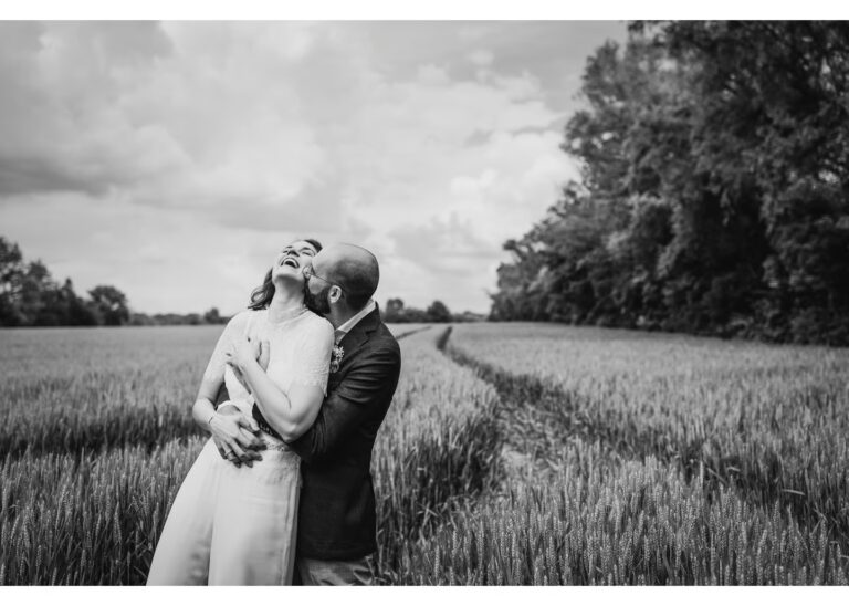 Brautpaar umarmt sich lachend in einem Feld während eines Hochzeitsshootings