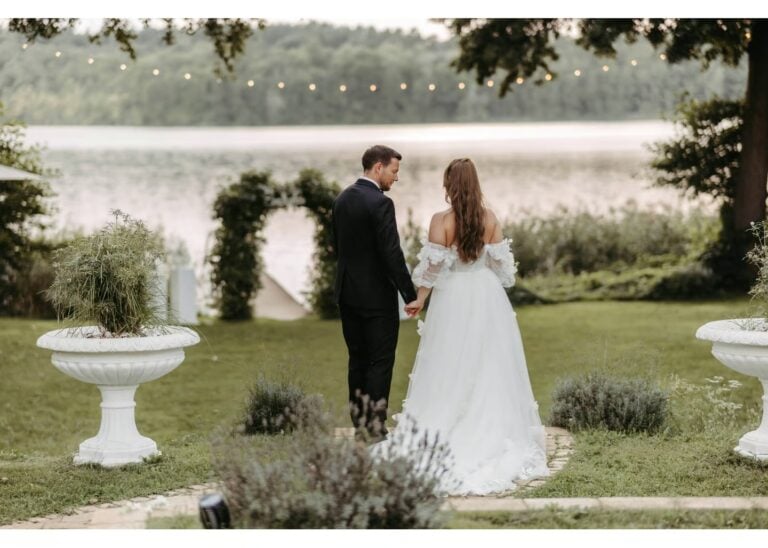 Brautpaar spaziert Hand in Hand durch einen Garten am See bei der Hochzeit