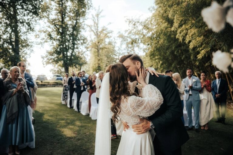 Braut und Bräutigam küssen sich während ihrer Outdoor-Hochzeitszeremonie vor den Gästen