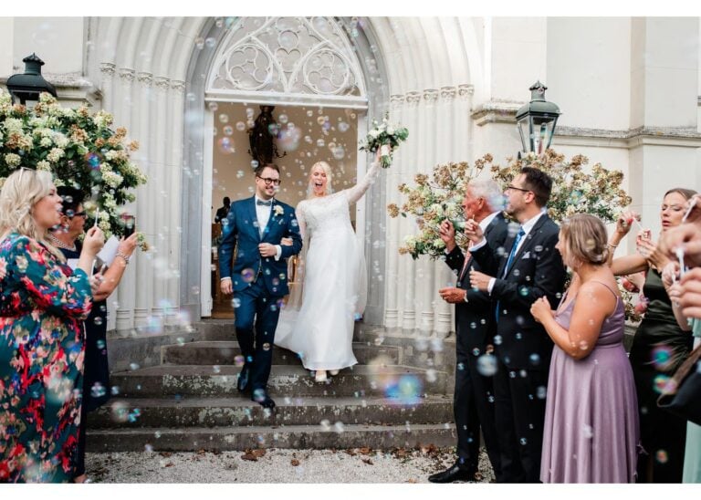 Braut und Bräutigam verlassen die Kirche nach der Trauung während Hochzeitsgäste Seifenblasen pusten