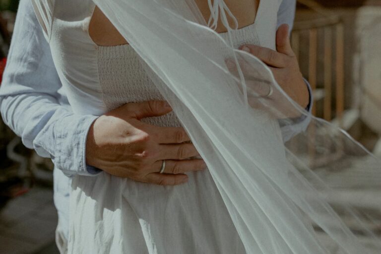 Bräutigam legt die Hände um die Taille der Braut, ihr Schleier weht im Wind