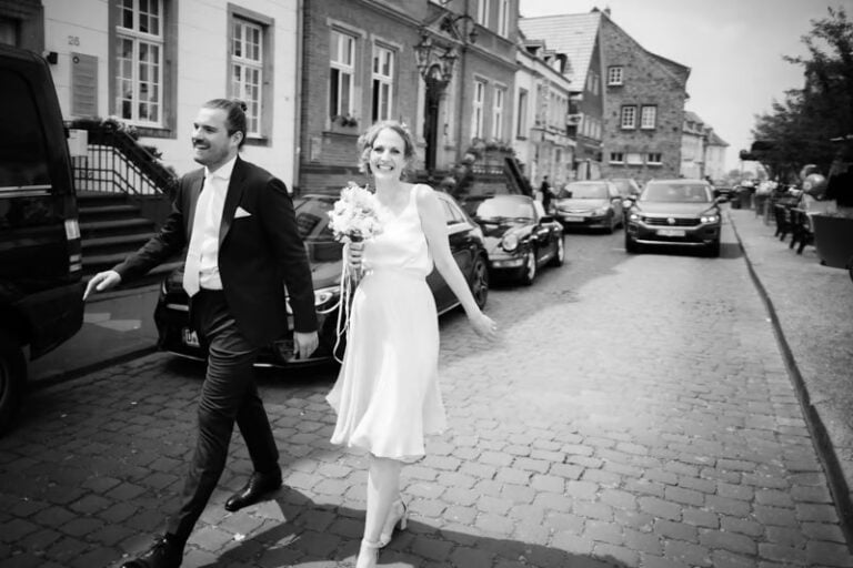 Braut und Bräutigam gehen lachend durch eine Altstadtstraße nach der Trauung