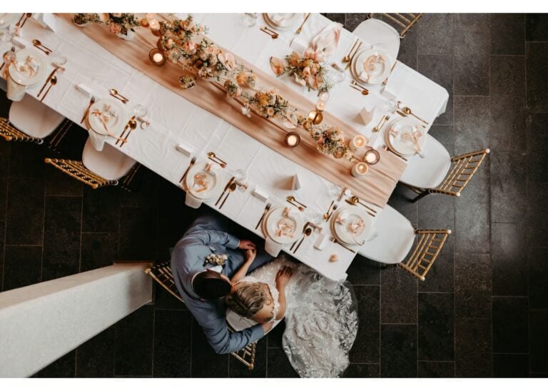 Brautpaar sitzt eng beieinander an einer festlich gedeckten Hochzeitstafel von oben fotografiert
