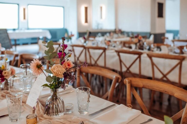 Stilvolle Hochzeit Tischdeko mit Blumenarrangement und rustikalen Holzstühlen im festlich gedeckten Saal