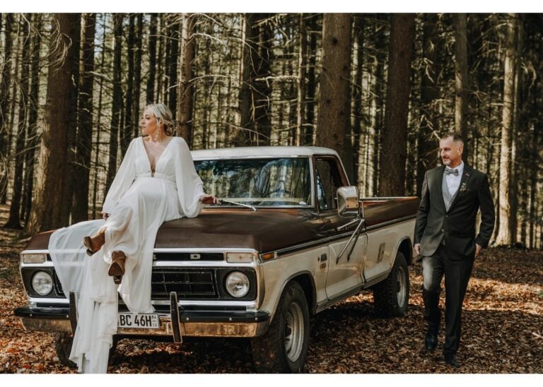 Braut sitzt auf einem Vintage-Pick-up im Wald, während der Bräutigam daneben läuft
