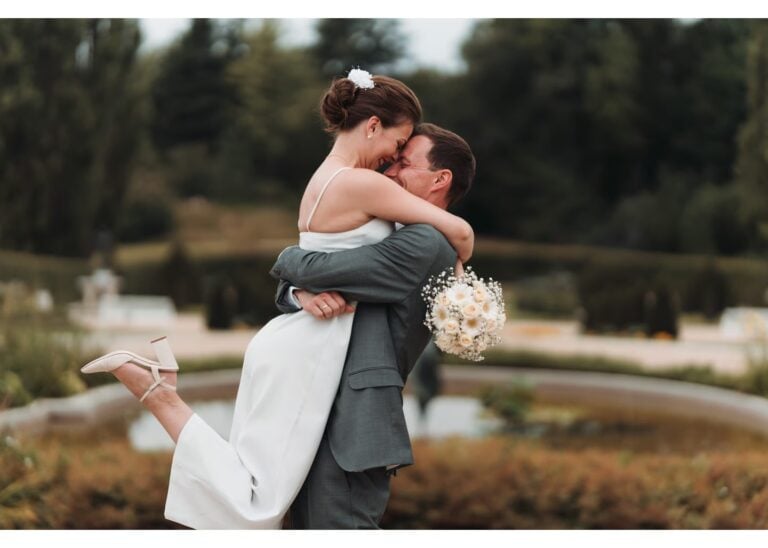 Bräutigam hebt seine Braut vor einem Brunnen im Park während der Hochzeit hoch
