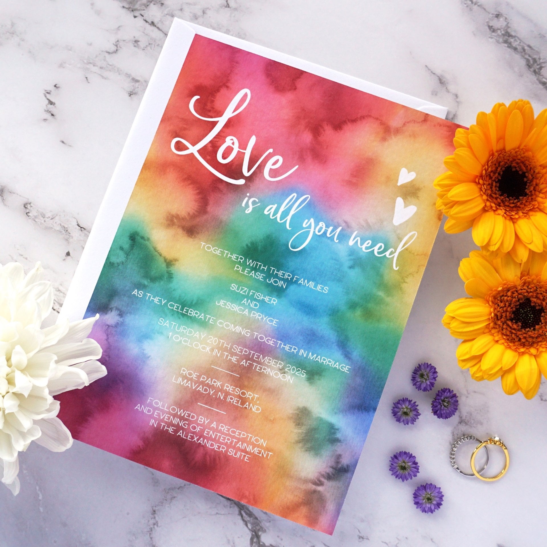 a rainbow watercolour wedding invitation that reads, 'love is all you need'