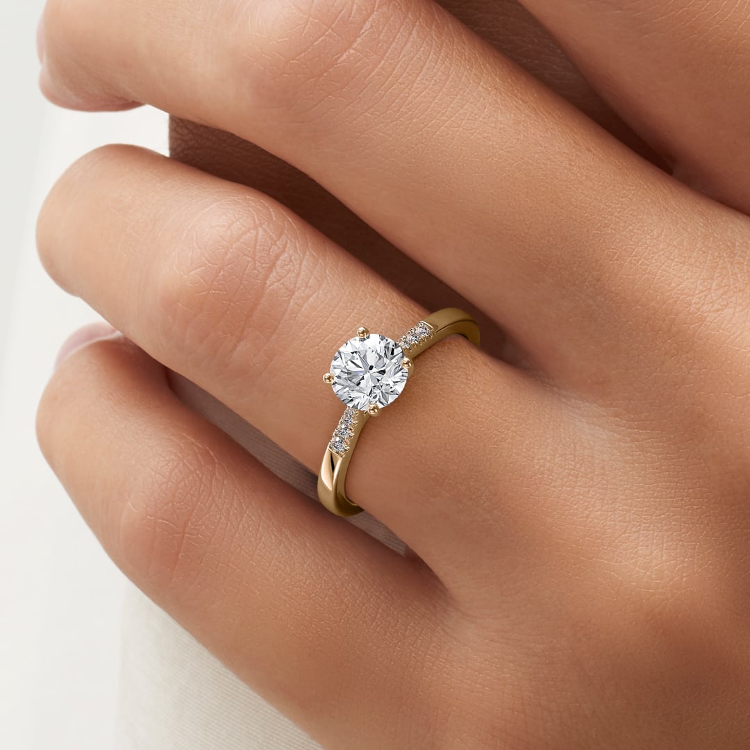 a close up of a hand wearing a round-cut diamond engagement ring in yellow gold