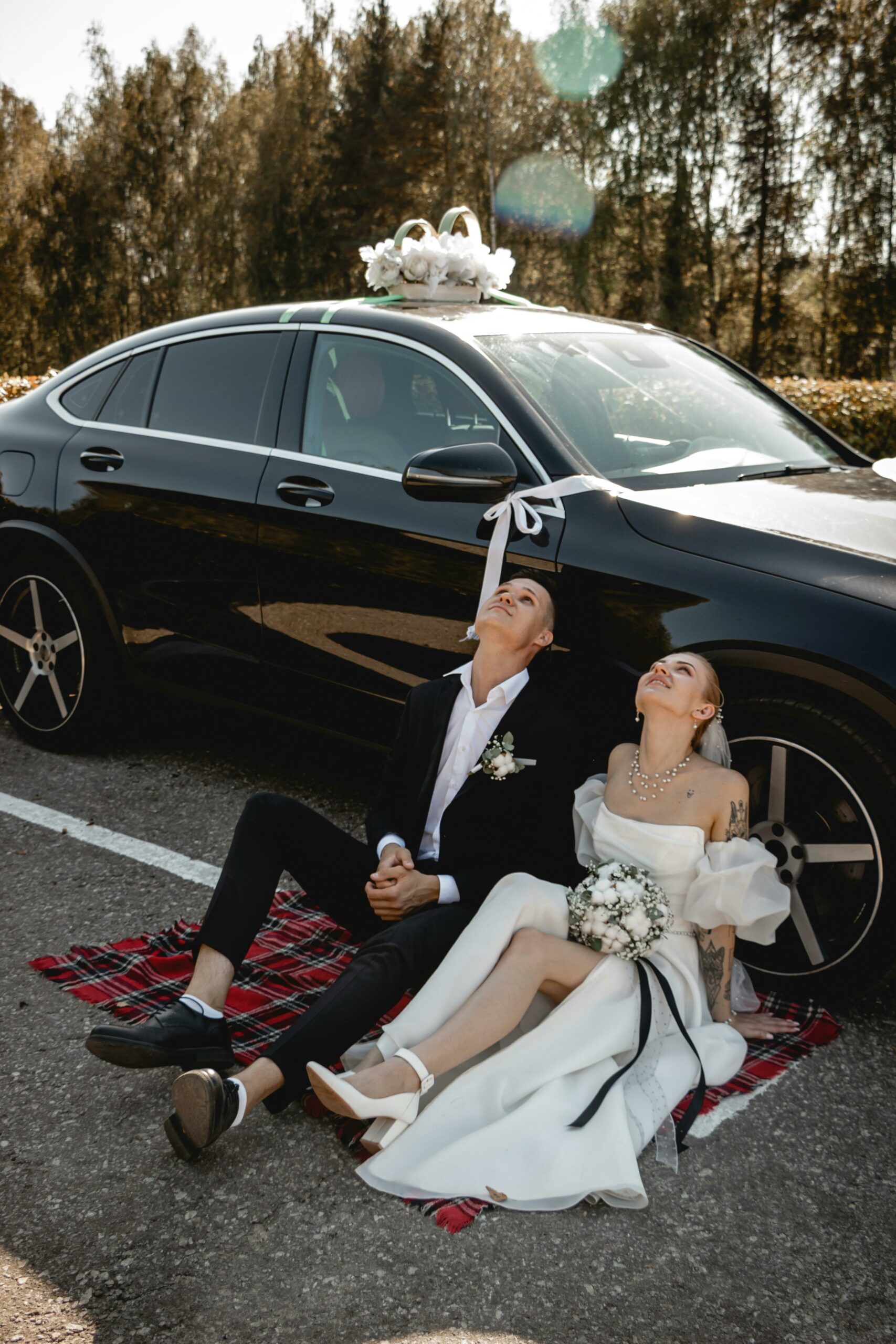 Bride and groom leaning against a luxury wedding car and looking at the sky
