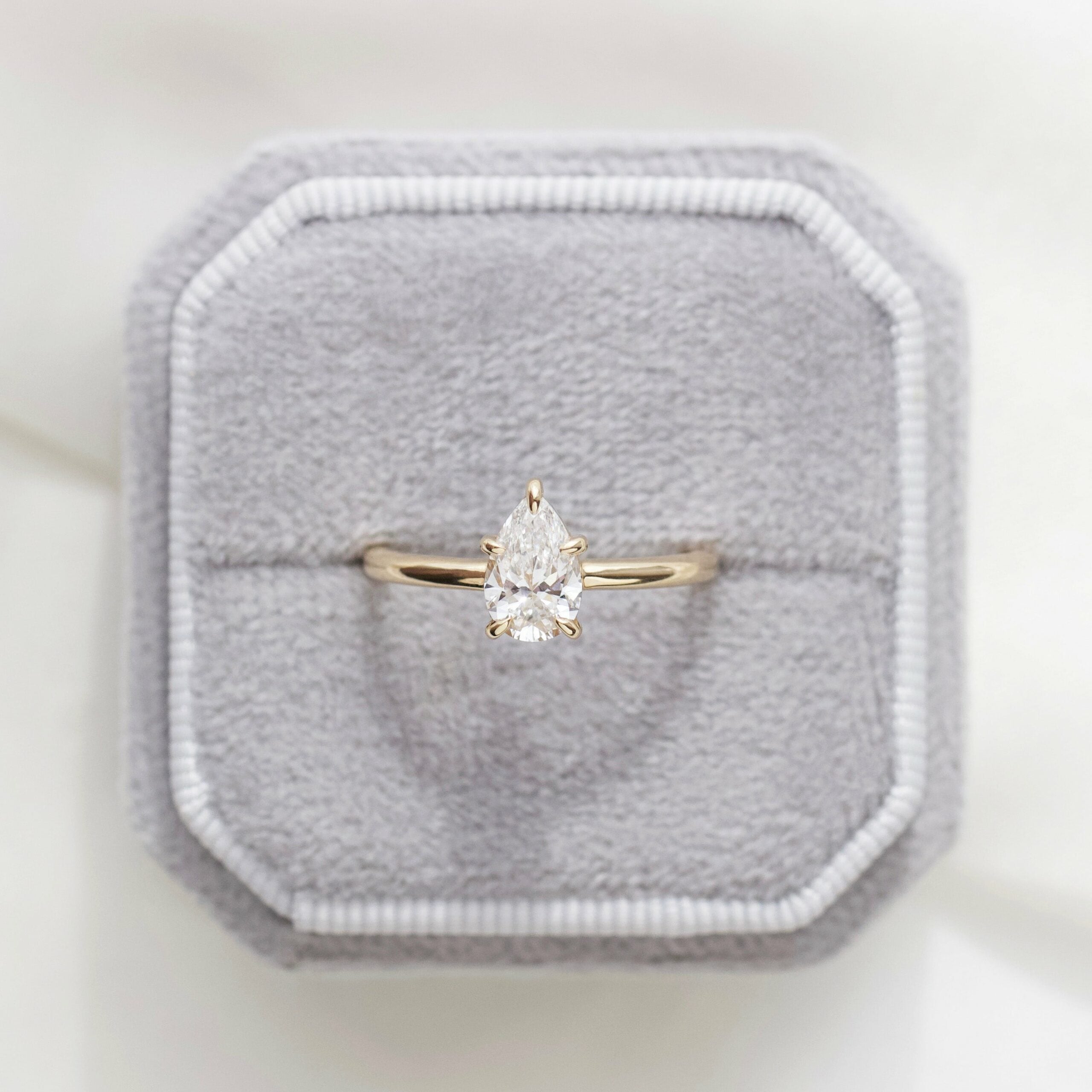 a pear-cut diamond ring on a yellow gold band tucked inside a grey cushioned ring box