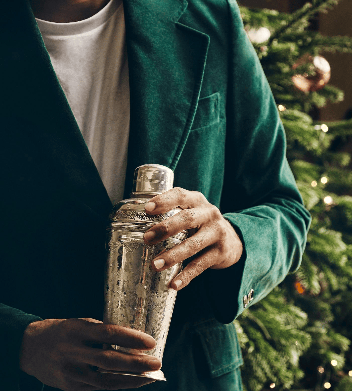 Man in a green velvet jacket holding an engraved silver cocktail shaker