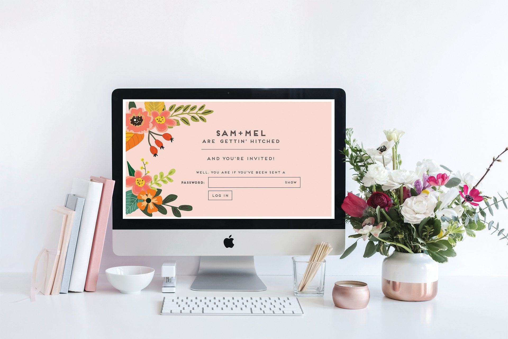 a tidy desk featuring a computer screen with digital wedding invitation, surrounded by various items including a vase of flowers and some books